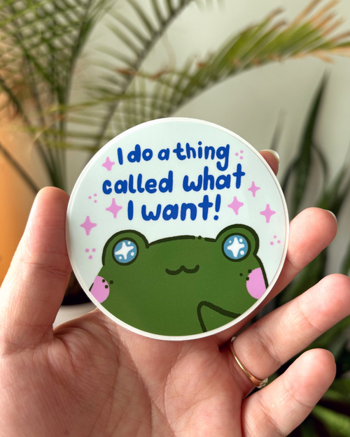 Easy Peel vinyl sticker with green frog that has light blue sparkly eyes, freckles and blush. Quote that says "I do a thing called what I want" in blue hand lettered text on a light green background surrounded by bubblegum pink sparkles