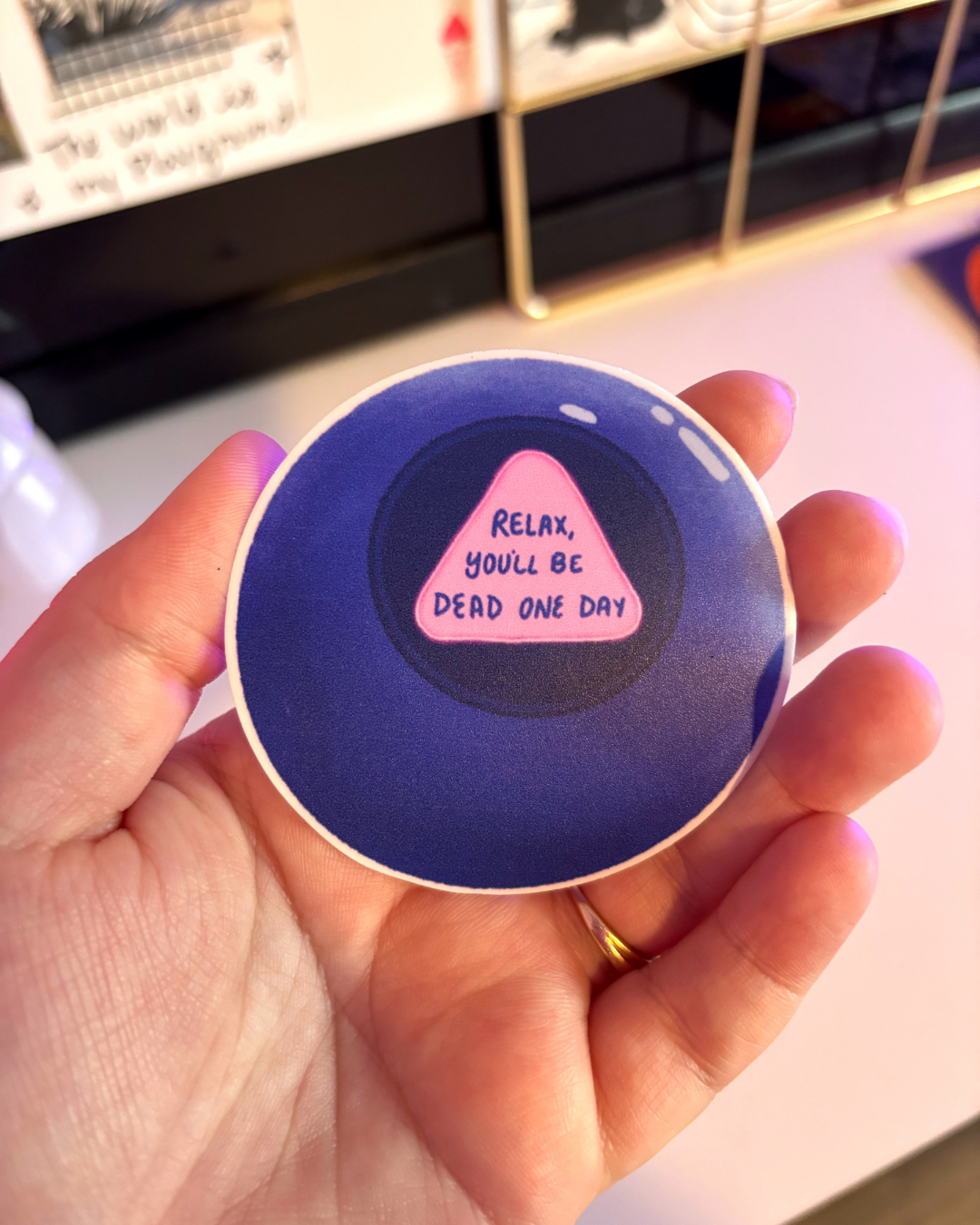 Dark blue magic 8 ball vinyl sticker featuring a future prediction in a pink triangle that says "relax, you'll be dead some day" 