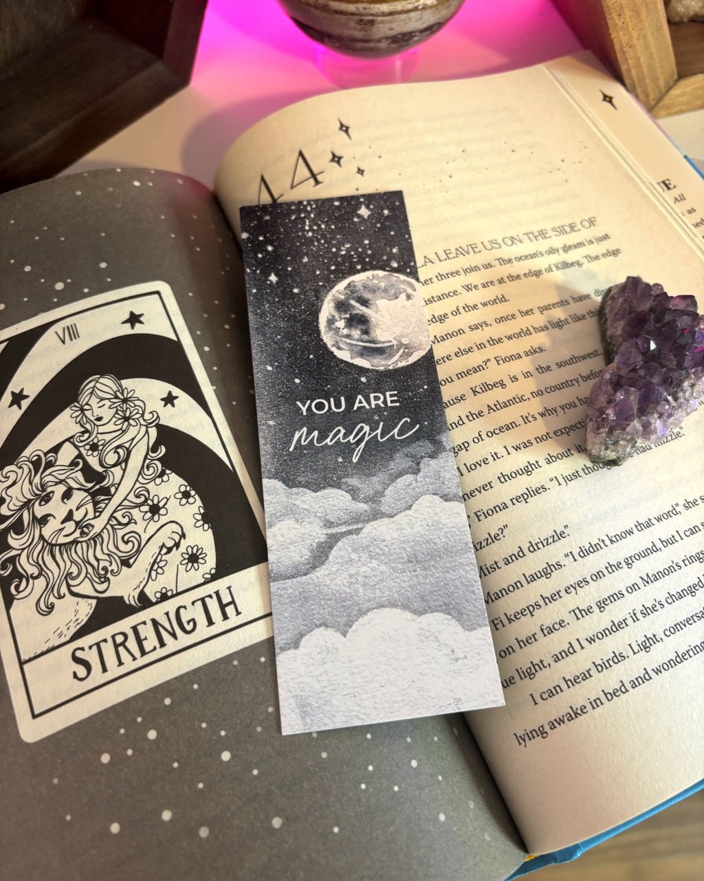 Book with a 'You are magic' bookmark, tarot card, and crystal on an open book