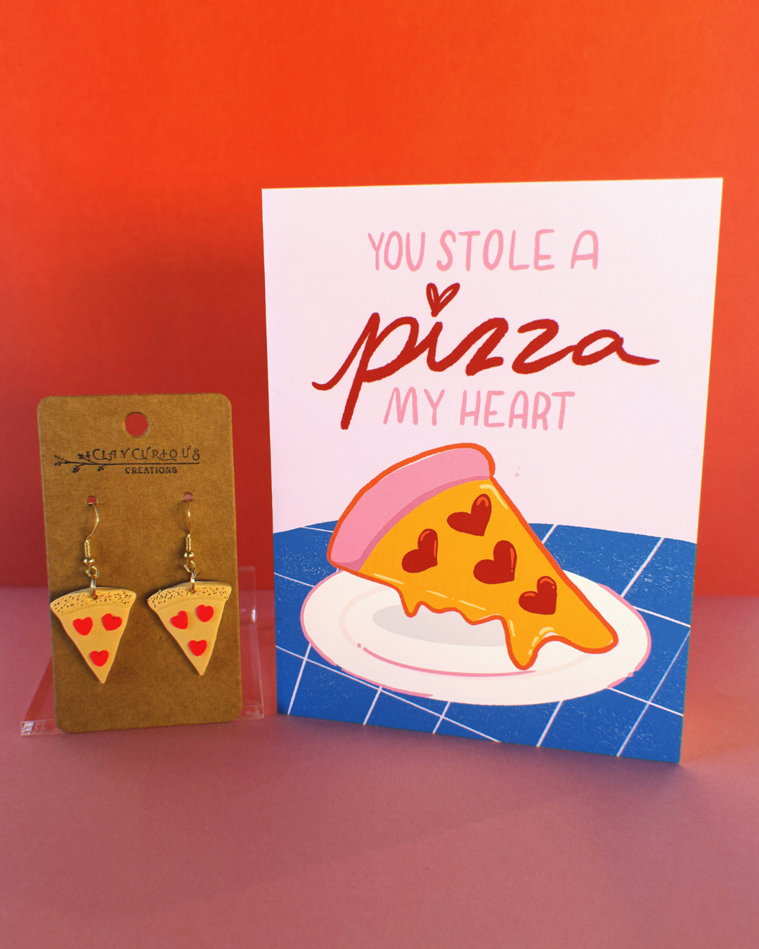 You stole a pizza my heart greeting card and a pair of polymer clay pizza slice earrings that have hot pink heart pepperonis.